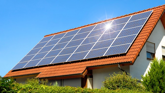 Solar panel on a red roof reflecting the sun and the cloudless blue sky